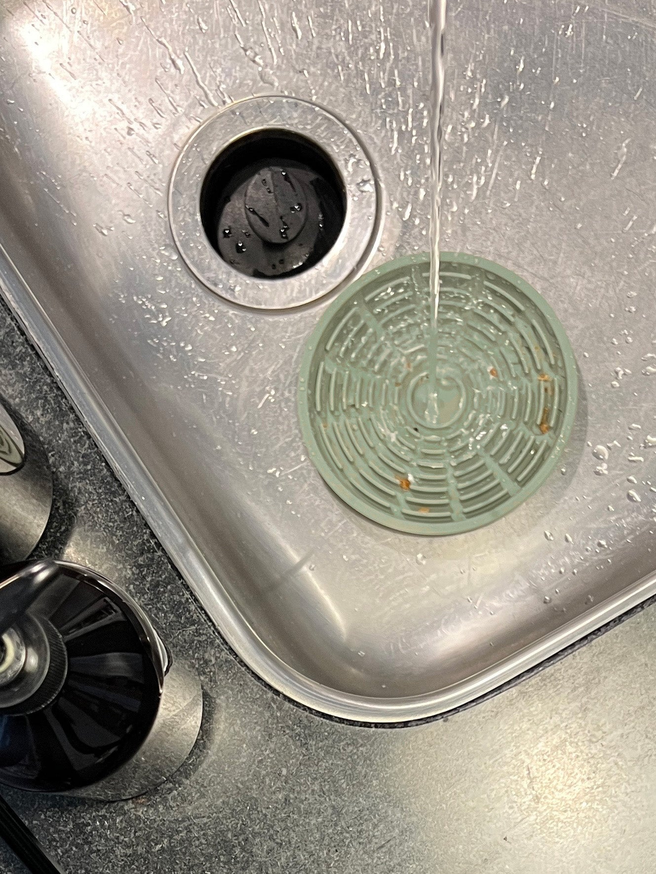 A green silicone lick mat sitting under a stream of water in a stainless steel sink
