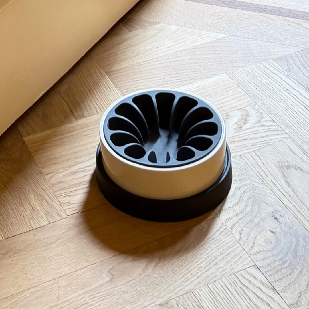 dark gray silicone slow feeder in cream and black porcelain pet dish on a herringbone oak wood floor