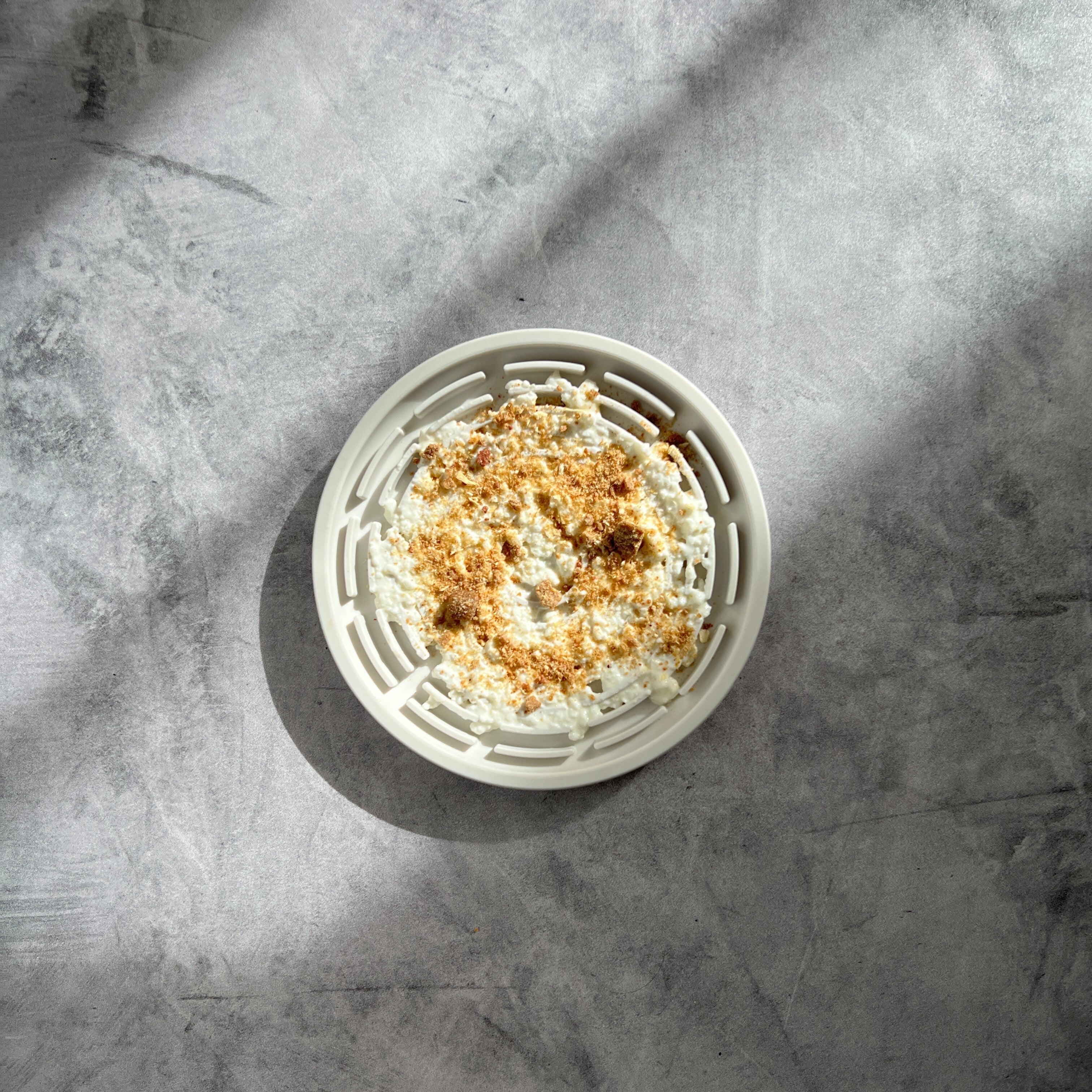 A white silicone lick mat filled with cottage cheese and treat crumbs